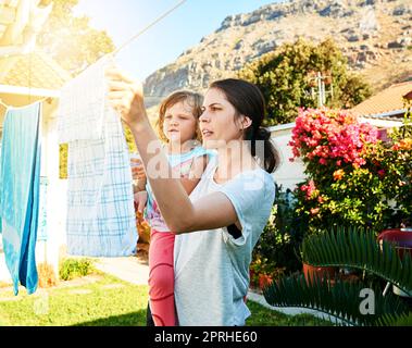 Lernen Sie den Job von Müttern kennen. Eine Mutter und Tochter hängen draußen zusammen Wäsche auf. Stockfoto