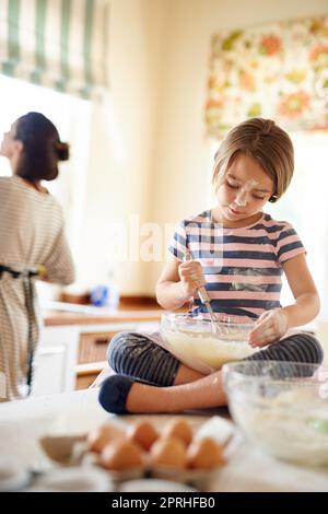 Mummys Küchenhelfer. Ein kleines Mädchen hilft ihrer Mutter in der Küche zu backen. Stockfoto