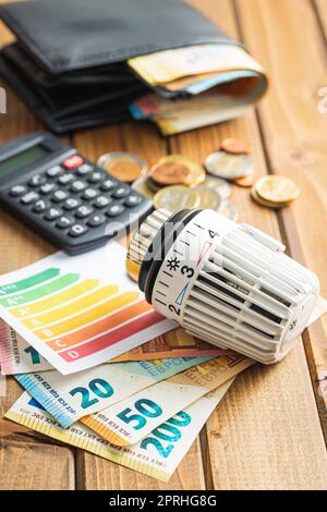 Thermostatischer Ventilkopf, Euro-Geld- und Energieetikett auf Holztisch. Konzept steigender Heizpreise. Stockfoto