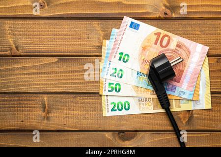 Elektrostecker und Euro-Geld auf Holztisch. Konzept steigender Strompreise. Stockfoto