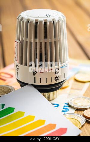 Thermostatischer Ventilkopf, Euro-Geld- und Energieetikett auf Holztisch. Konzept steigender Heizpreise. Stockfoto