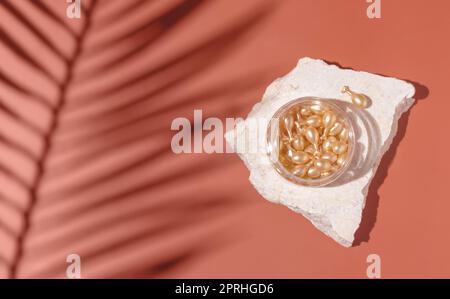 Sehen Sie Serumkapseln in einem Glas auf Stein auf rosa Draufsicht, Palmenblätter harte Schatten. Schönheitsprodukt Stockfoto