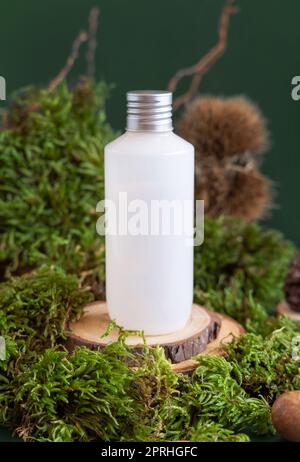 Weiße cremefarbene Plastikflasche auf einem Holzstück zwischen grünem Moos, Nahaufnahme, natürliches kosmetisches Modell Stockfoto