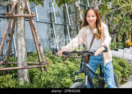 Glückliche asiatische wunderschöne junge Frau, die auf der Straße in der Nähe von Building City Fahrrad fährt Stockfoto
