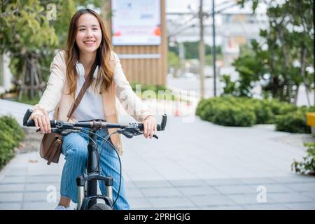 Glückliche junge asiatische Frau, die Fahrrad auf der Straße in der Nähe von Building City fährt Stockfoto