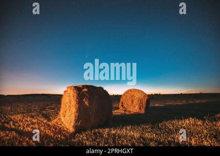 Comet Neowise C2020 F3 in Night Starry Sky über Heuhaufen im Summer Agricultural Field. Nachtstars Über Der Ländlichen Landschaft Mit Heuballen Nach Der Ernte. Landwirtschaftskonzept Stockfoto