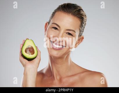 Natürliche Hautpflege, ältere Frau mit Avocado und glückliches Studioporträt. Gesichtsbehandlung, Ernährung in grünen Früchten und eine gesunde Lebensweise. Bio-Lebensmittel Stockfoto