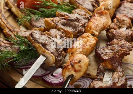 Verschiedene gegrillte Fleischsorten. Schaschlik aus verschiedenen Fleischsorten auf Grillspießen mit Gemüse und Lavash auf Holzbrett. Draufsicht. Lebensmittelhintergrund. Servin Stockfoto