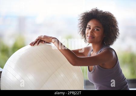 Das ist mein Fitnessgeheimnis. Ein Porträt einer attraktiven jungen Frau, die mit einem Gymnastikball sitzt Stockfoto