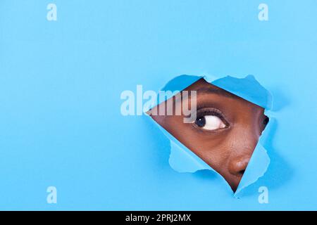 Ist da etwas? Ein Blick auf ein Frauenauge, das durch ein Loch in einem bunten Papier schaut Stockfoto