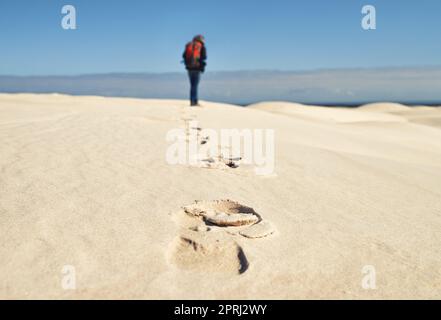 Hinterlässt Spuren. Rückansicht einer jungen Wanderin, die entlang der Sanddünen läuft Stockfoto