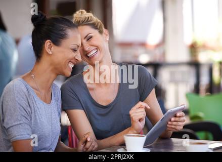 Technologie bringt Menschen näher. Zwei junge Frauen, die in einem Café ein Tablet betrachten Stockfoto