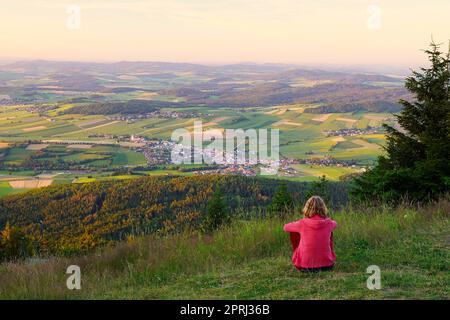 Eine Frau, die auf dem Berg Hohenbogen sitzt und nach Neukirchen Heiligblut schaut, einer kleinen Stadt im Bayerischen Wald. Stockfoto