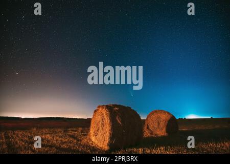 Comet Neowise C2020 F3 in Night Starry Sky über Heuhaufen im Summer Agricultural Field. Nachtstars Über Der Ländlichen Landschaft Mit Heuballen Nach Der Ernte Stockfoto