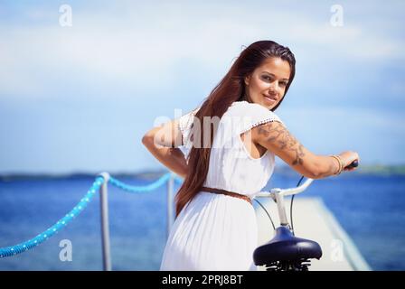 Eine wunderschöne tätowierte junge Frau, die ihr Fahrrad an einem Pier entlang schiebt Stockfoto