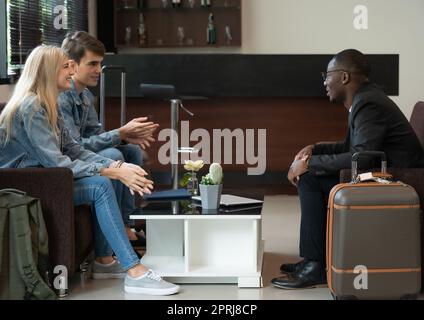 Lächelnde, vielfältige Reisende, die in der Flughafenlounge sitzen und sich unterhalten. Stockfoto