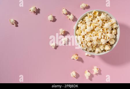 Popcorn in einer weißen Schüssel auf pinkfarbenem Hintergrund. Stockfoto