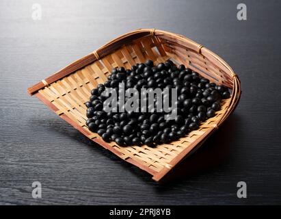 Schwarze Sojabohnen in einem Sieb vor schwarzem Hintergrund. Stockfoto