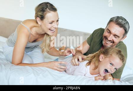 Glückliche Familie, Bett und Spaß Familie spielen und lachen, während mit kleinen Mädchen in einem Schlafzimmer entspannen. Glückliche, verspielte und liebevolle Eltern, die albern damit sind Stockfoto