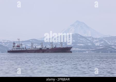 Kamtschatka Halbinsel, Russland. Seehafen in Petropavlovsk-Kamtschatsky. Schiffe im Straßenstead vor dem Hintergrund des Vulkans Stockfoto