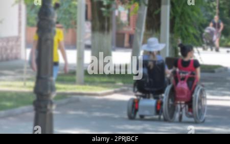 Verschwommener Blick auf zwei Behinderte auf einem elektrischen Rollstuhl auf einer Straße der Stadt. Stockfoto