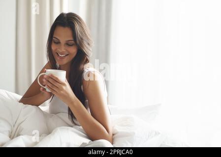 Sie beginnt ihren Tag mit Koffein. Eine schöne junge Frau, die eine Tasse Kaffee im Bett genießt Stockfoto