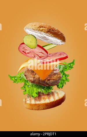 Burger mit fliegenden Zutaten isoliert auf orangefarbenem Hintergrund Stockfoto