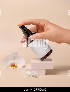 Eine Frau pumpt Flüssigkeit aus einer Kosmetikflasche neben Orchideenblumen auf beige Nahaufnahme, Etikettenmodell. Produktpaket für Hautpflegeprodukte, minimale Komplettleistung Stockfoto