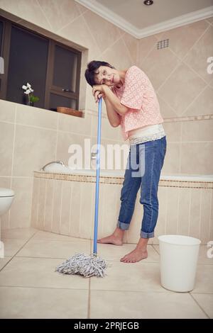 Müde von der Hausarbeit. Eine müde aussehende Frau, die einen Badezimmerboden wischt. Stockfoto