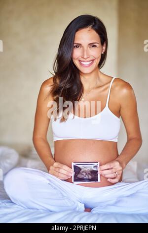 Babys erstes Porträt. Porträtaufnahme einer Schwangeren, die ein Sonogramm vor ihrem Bauch hält. Stockfoto