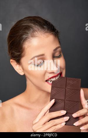 Shes ein Liebhaber von Schokolade. Studioaufnahme einer attraktiven jungen Frau, die von etwas Süßem verlockt wird. Stockfoto