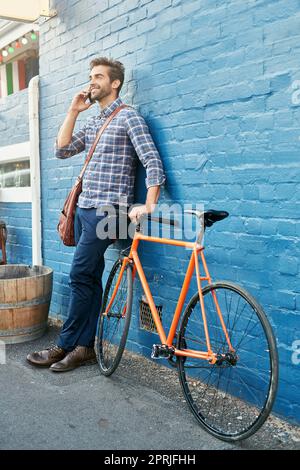 Ich rollte gerade zum Café. Ein hübscher junger Mann lehnte sich mit seinem Fahrrad an einer Wand und sprach auf einem Handy. Stockfoto