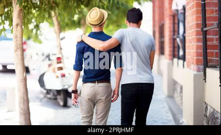 Liebe lässt deine Seele aus ihrem Versteck kriechen. Rückansicht eines schwulen Paares, das die Straße entlang läuft Stockfoto