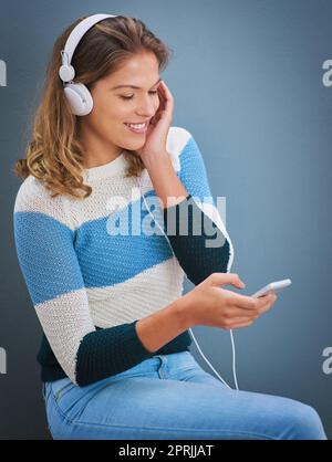 Gute Gefühle kommen von guten Liedern. Studioaufnahme einer jungen Frau, die vor grauem Hintergrund Musik hört. Stockfoto