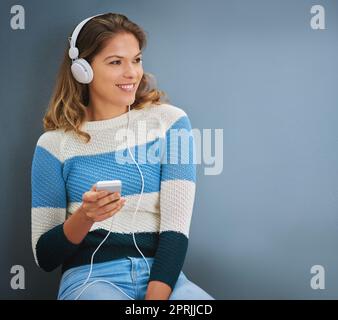 Einige ihrer besten Erinnerungen stammen aus Songs. Studioaufnahme einer jungen Frau, die vor grauem Hintergrund Musik hört. Stockfoto