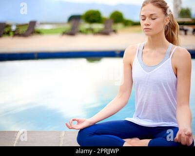 Ihre innere Ruhe finden. Eine junge Frau, die Yoga neben einem Pool draußen macht. Stockfoto