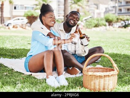 Ein Paar beim Picknick, eine Schwarze und eine Flasche Bier zusammen. Junger afrikanischer Mann, Alkohol trinken und glückliches Mädchen. Natur im Freien, Park in der Stadt und Zeit für eine Beziehung Stockfoto