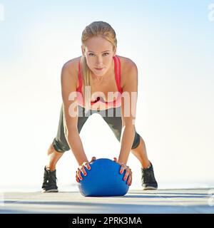 Sie nimmt ihre Fitness ernst. Ganzkörperportrait einer jungen Frau, die Liegestütze mit einem Medizinball macht. Stockfoto
