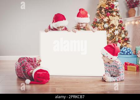 Vier Kinder drinnen mit leerem Banner an Weihnachten. Konzept von Postkarte, Banner und Info. Stockfoto