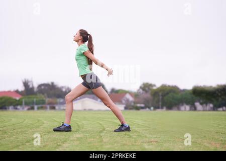 Aufwärmen für ein intensives Workout. Eine junge Frau, die sich auf einem grasbedeckten Feld streckt Stockfoto