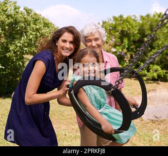 Lass mich hoch gehen. Ein kleines Mädchen, das draußen auf eine Schaukel geschubst wird Stockfoto