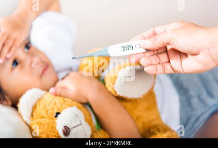 Krankes Kind. Mutter Eltern überprüfen die Temperatur ihrer kranken Tochter mit einem Digitalthermometer im Mund, Kind liegt im Bett und misst ihre Temperatur Stockfoto