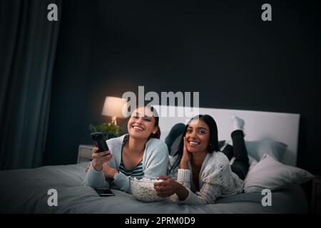 Wir lieben Chick-Flick-Nächte. Zwei junge Frauen essen Popcorn, während sie sich zu Hause einen Film ansehen Stockfoto