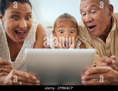 Tablet, Familie und schockiert Gesicht Kind Blick auf Video Online-Verbindung zu Hause. Wow Großeltern, junge Mädchen und Spaß Aktivität Streaming Film oder Stockfoto