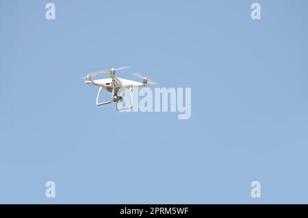 Big White drone schwebt in einem hellen wolkenlosen blauen Himmel, Radio Control Helicopter mit tragbaren Videokamera Versorgung Stockfoto
