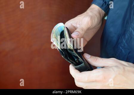 Mann hält in der Hand schwarzes Leder-Etui mit ukrainischen Geld oder Dieb, der Tasche voller Geld gestohlen hat. Ukrainische Wirtschaftskrise und Kriminalität Konzept Stockfoto