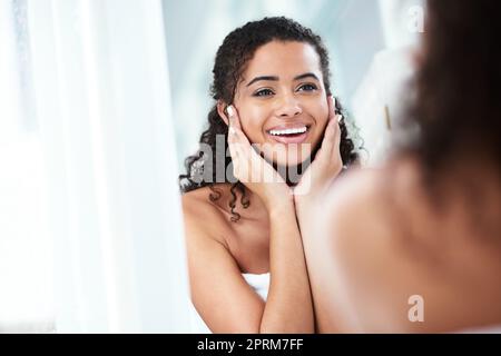 Glühende Haut träumt jede Frau. Eine wunderschöne junge Frau, die erfreut aussah, während sie in den Badezimmerspiegel schaute Stockfoto