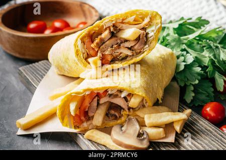 Rustikale Rolle Shawarma mit pommes frites, Champignons, Huhn und Gemüse in Pita-Brot auf dunklem Holzhintergrund mit Kirschtomaten und grünem pa Stockfoto