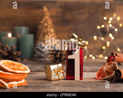 Kerze vom ersten Advent brennt, Holznummer 1 mit Geschenkschachteln, Tannenzapfen und Weihnachtsdekoration auf Holz mit Weihnachtslichtern Stockfoto