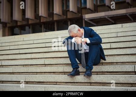 Nicht sein bester Tag. Ein niedergeschlagen Geschäftsmann sitzt auf der Treppe vor seinem Büro mit dem Kopf in den Händen. Stockfoto